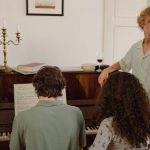A diverse group of adults gathered indoors playing and enjoying music around a piano.